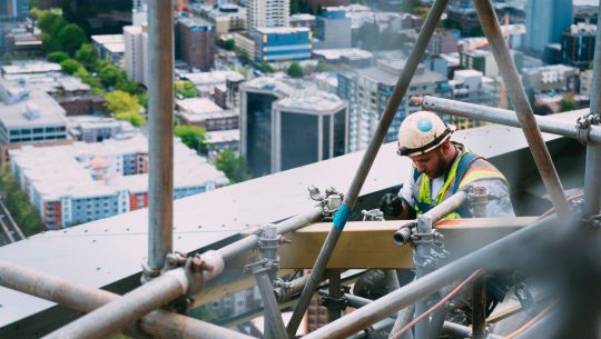 Bauarbeiter in großer Höhe auf Baugerüst, gesichert durch PSA gegen Absturz
